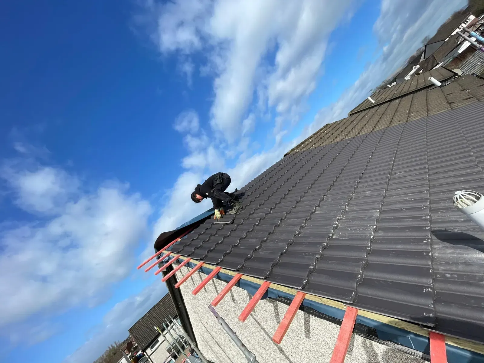 Roofer fitting ridge tiles against a clear blue sky in Falkirk