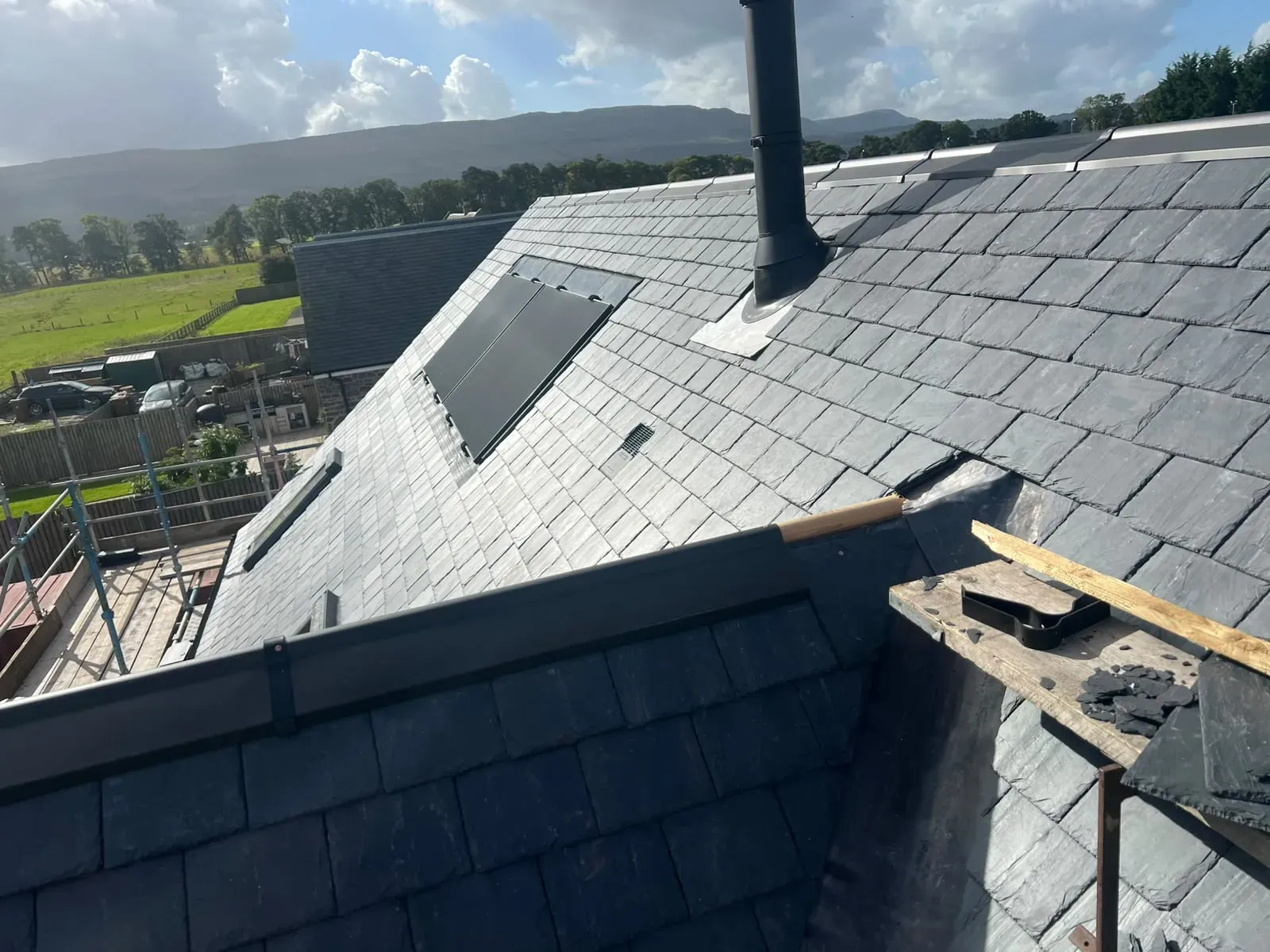 New slate roof with stove flue and roof window, countryside behind