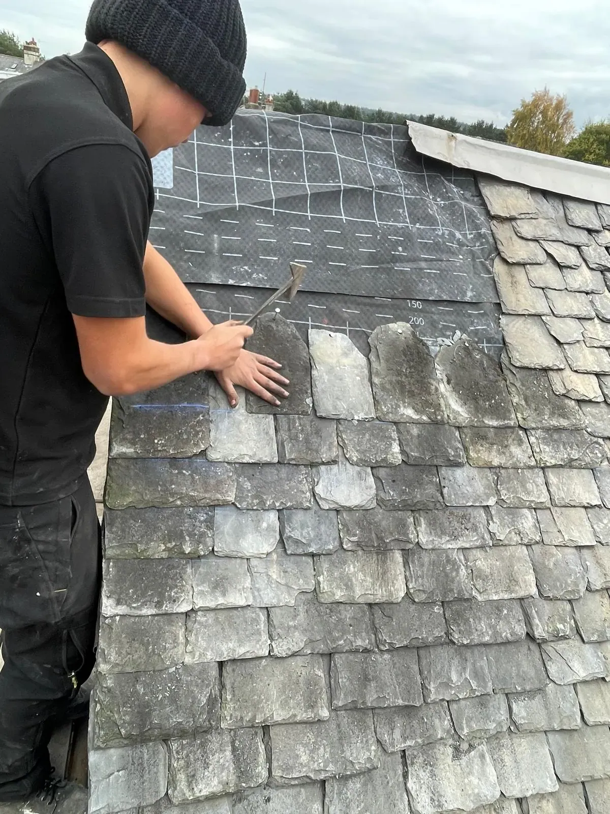 Close-up of an AGM roofer refitting reclaimed slate tiles in Falkirk
