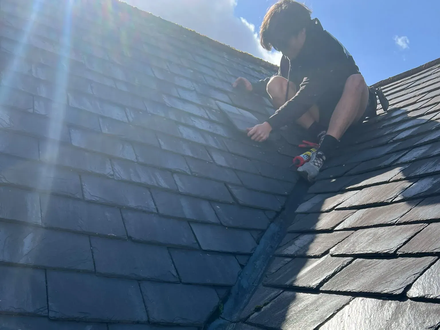 Roofer repairing slates beside a lead valley on a pitched slate roof