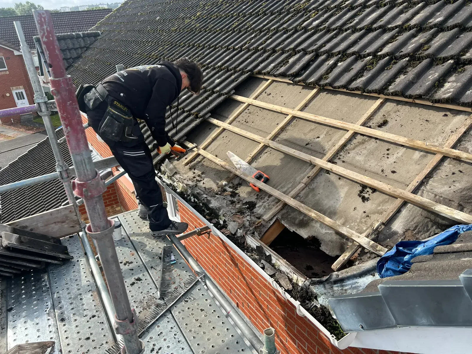 Roofer stripping old concrete tiles back to the battens to repair a damaged section